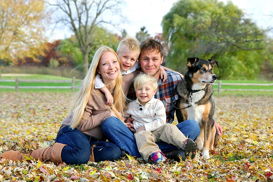 Blog - Happy Family Sitting In Field Of Leaves With Their Dog